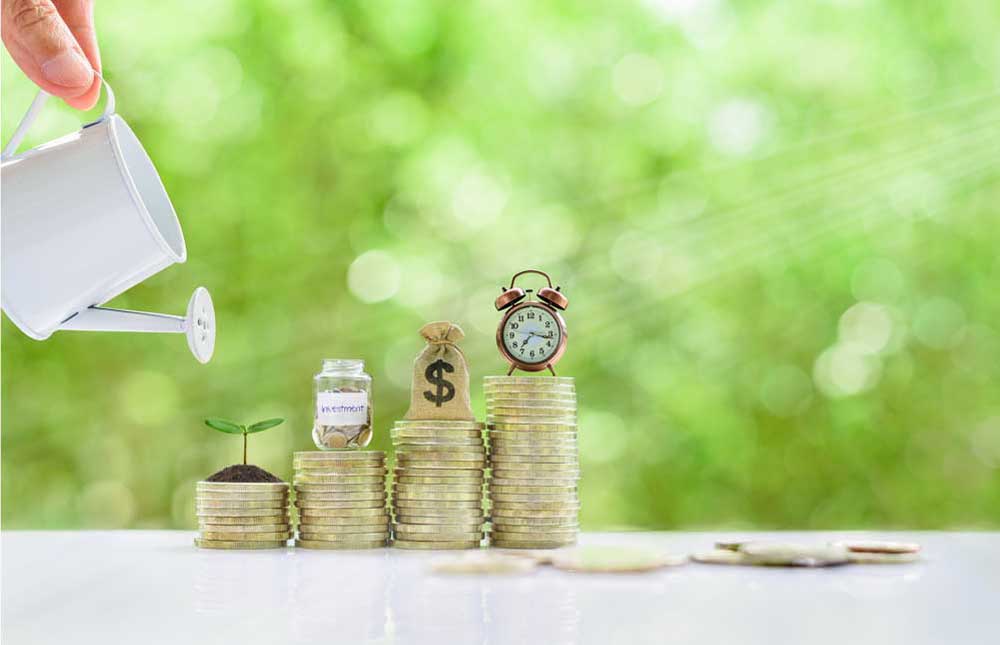 Long-tern investment, time value of money concept : Clock, US dollar bag, glass jar, a small tree on steps of rising coins. Hand pour water from a watering can, depicts asset growth from investment